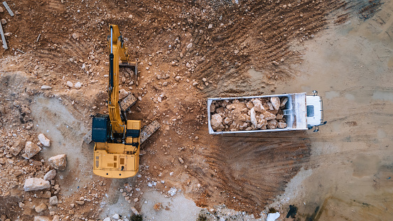 gettyimages-2192398535-170667a-3 Aerial view of heavy machinery loading rocks into a truck at a construction or mining site, showcasing efficient earthmoving and site preparation.