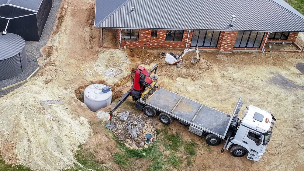 Aerial view of a septic tank installation beside a newly built brick house with construction equipment and a service truck on site.